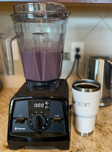 Image of Vitamix blender with purple smoothie made with celery, carrots, cucumber, blackberries, raspberries, protein powder, organic soy milk, and ice.